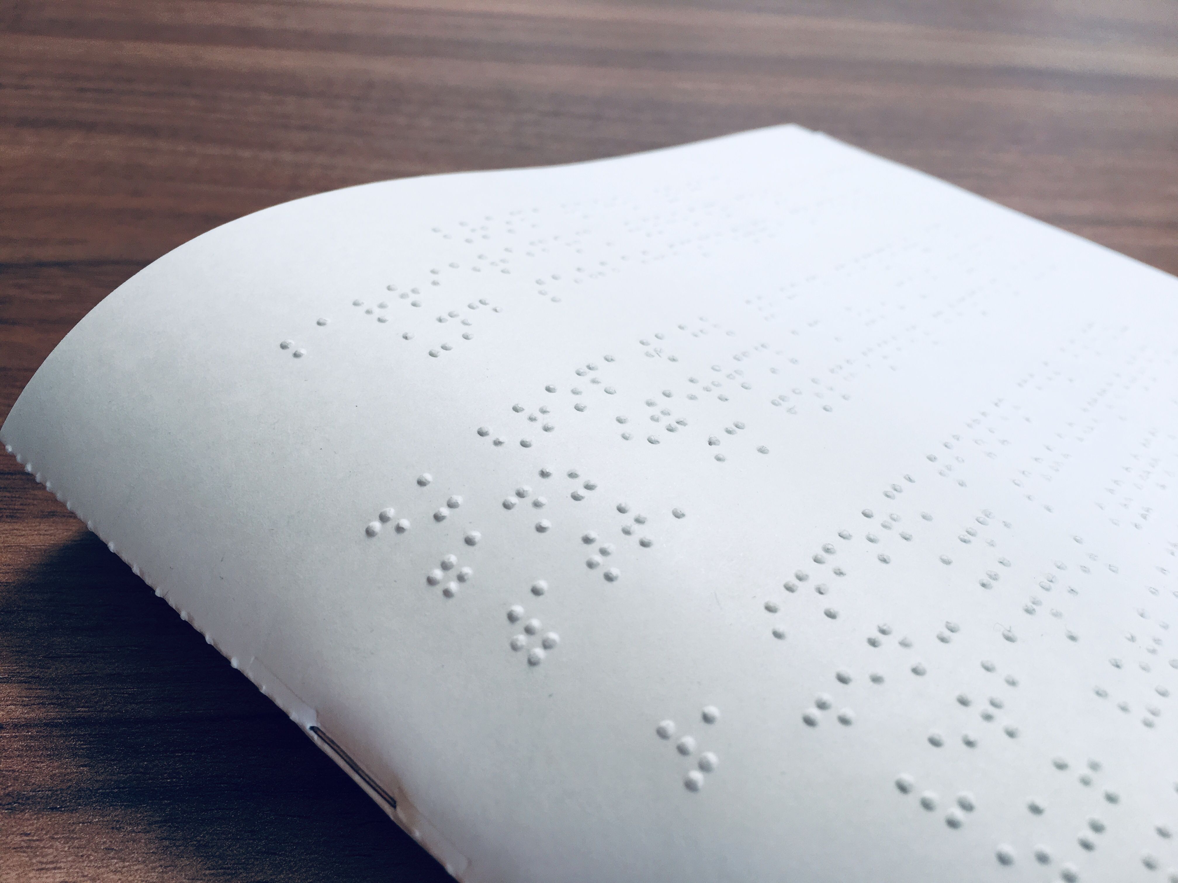 Ein Braillebogen liegt auf einem braunen Holztisch. 